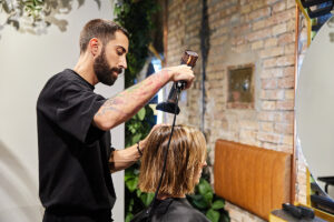 Male hairdresser drying the hair of a client sitting in front of a mirror in a modern hairdressing salon.