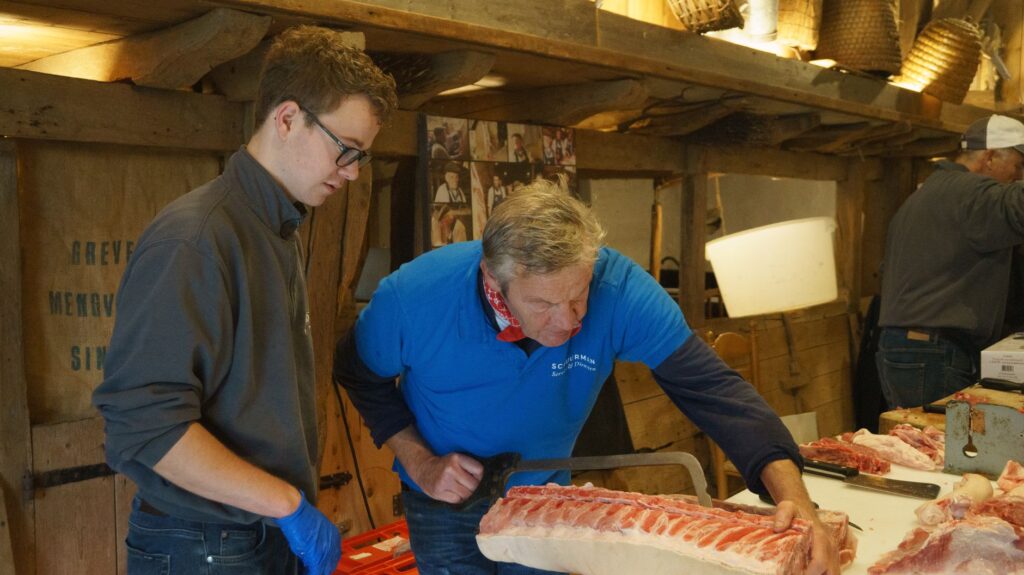 Deux professionnels de la boucherie preparent des pieces de viande en atelier, illustrant la transmission du savoir-faire du metier