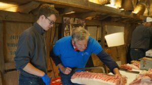 Deux professionnels de la boucherie preparent des pieces de viande en atelier, illustrant la transmission du savoir-faire du metier