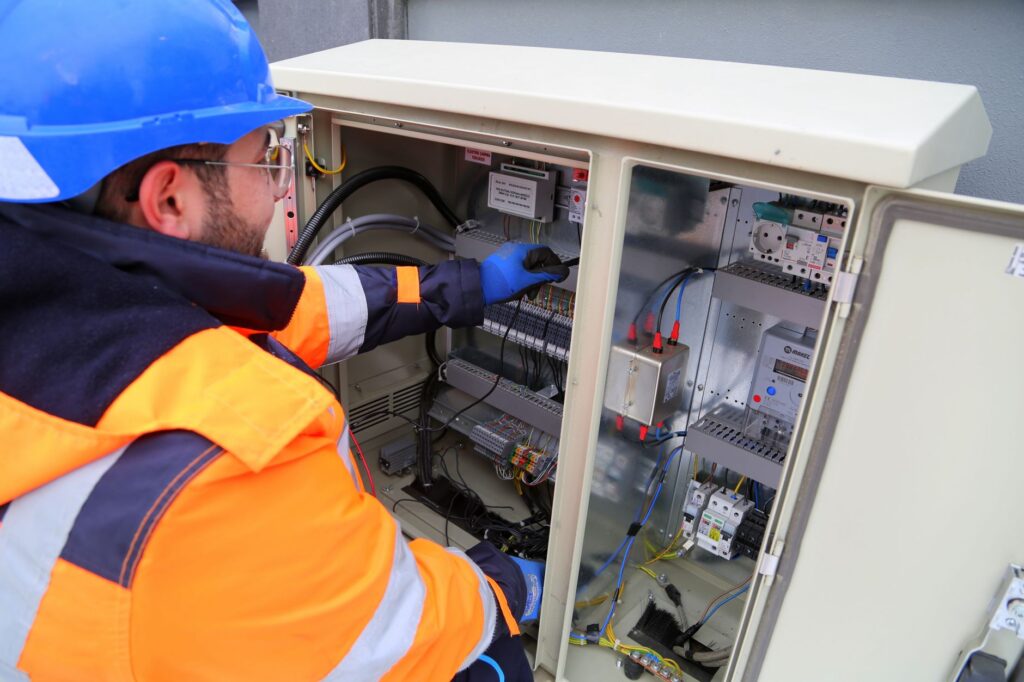 Électricien équipé d'un casque, d'un vêtement haute visibilité et de gants isolants intervenant sur une armoire électrique